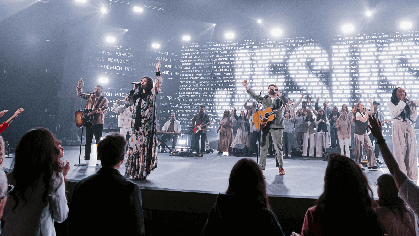 Personas adorando en el escenario con el nombre de Jesús detrás